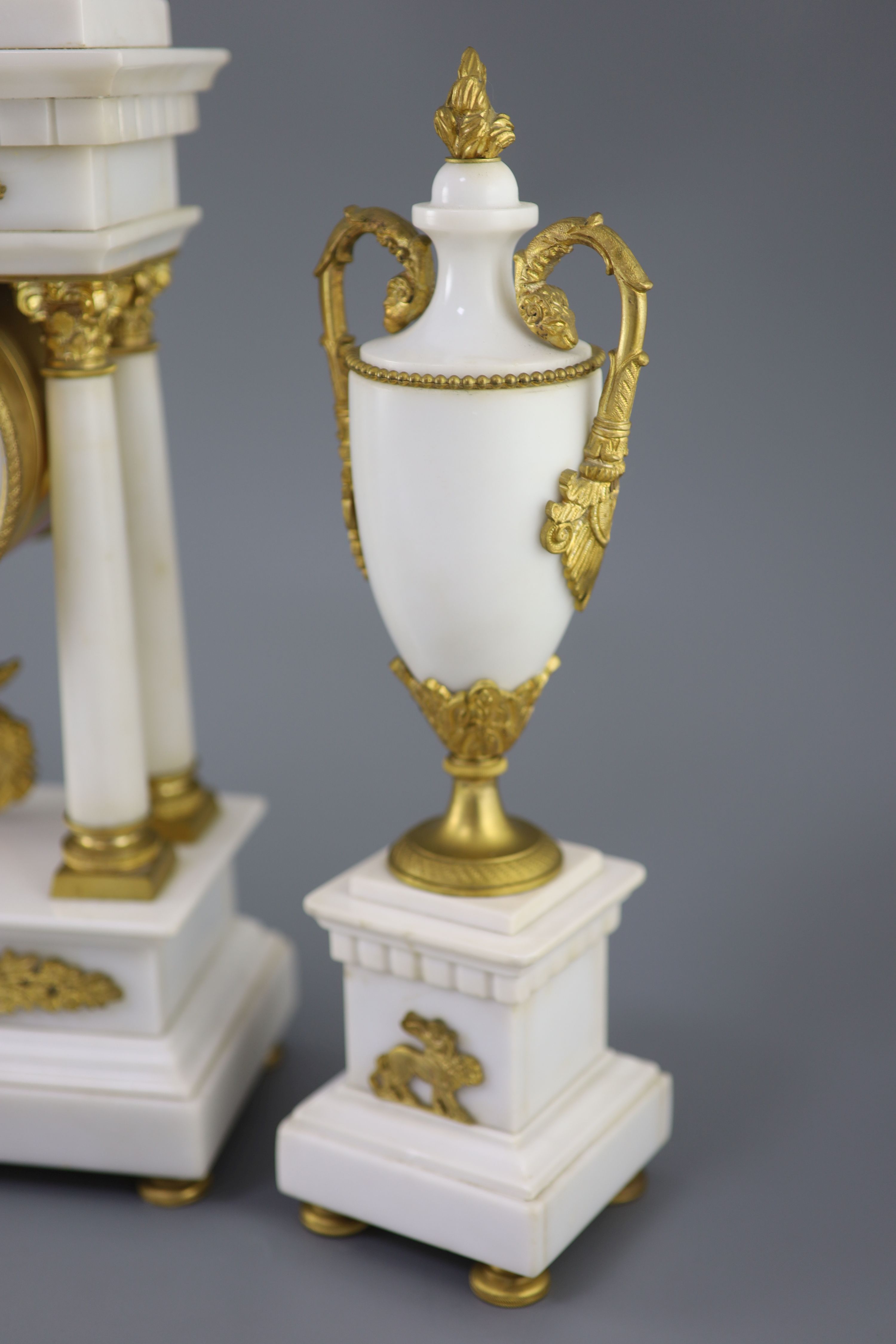 A Louis XVI style ormolu mounted white marble clock garniture, clock 14.5in. urns 13.75in.